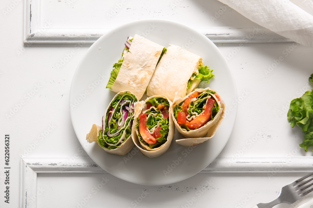 Plate of tasty lavash rolls with vegetables and greens on white wooden background