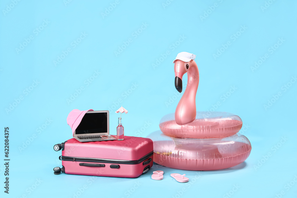 Suitcase with laptop and different beach accessories on blue background. Travel concept