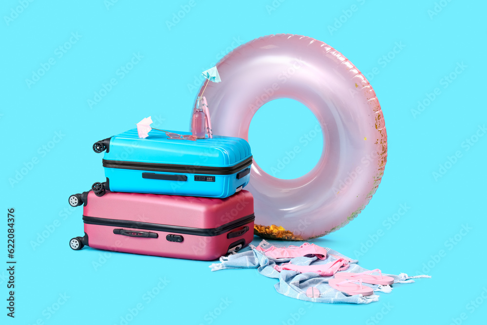 Suitcases with lemonade and different beach accessories on blue background. Travel concept