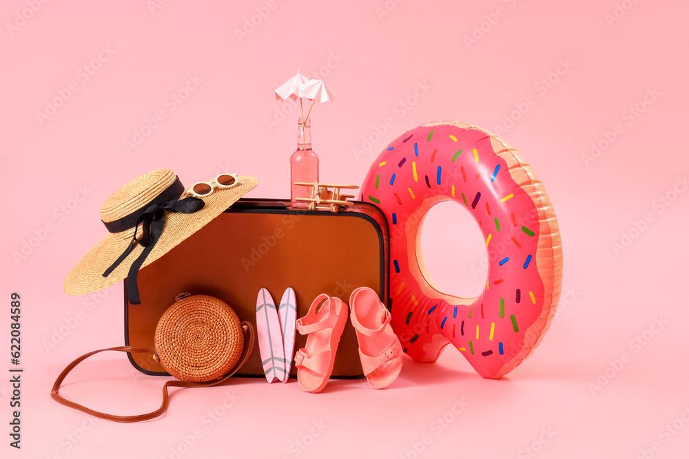 Suitcase with inflatable ring and beach accessories on pink background. Travel concept