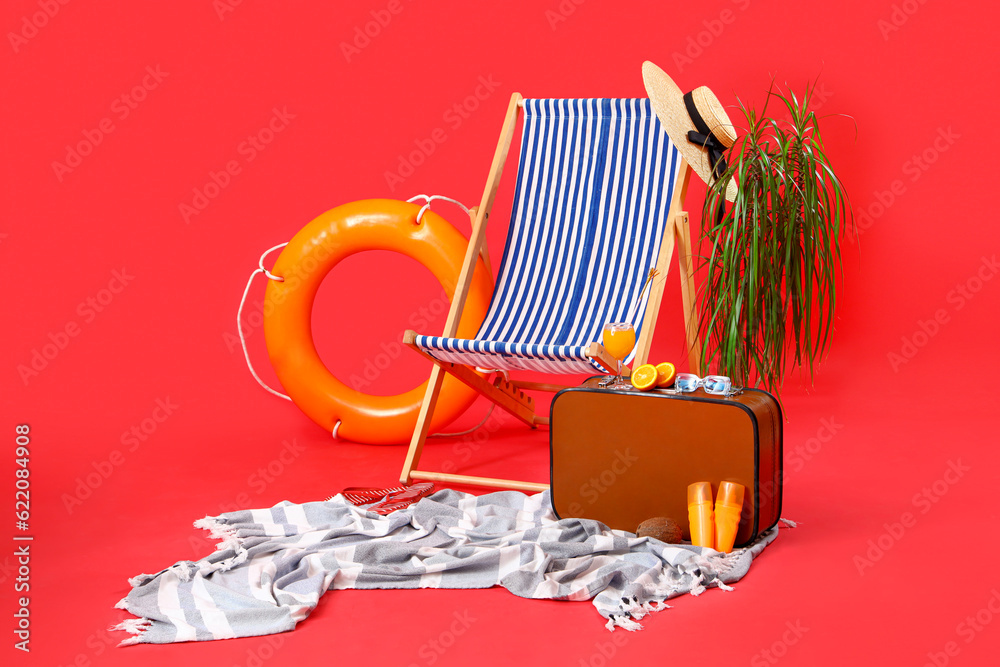 Deckchair with suitcase, ring buoy and different beach accessories on red background. Travel concept