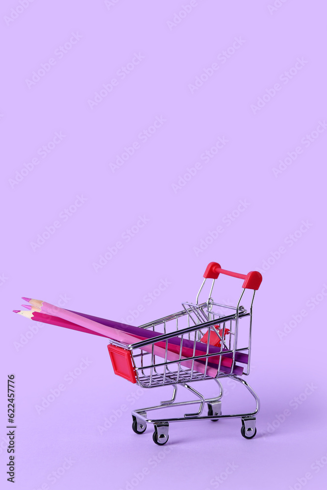 Shopping cart with color pencils on lilac background