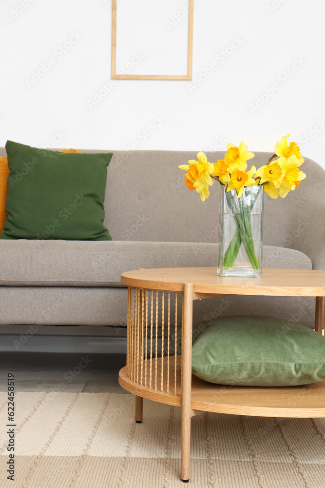 Vase with narcissus flowers on coffee table and grey sofa in living room