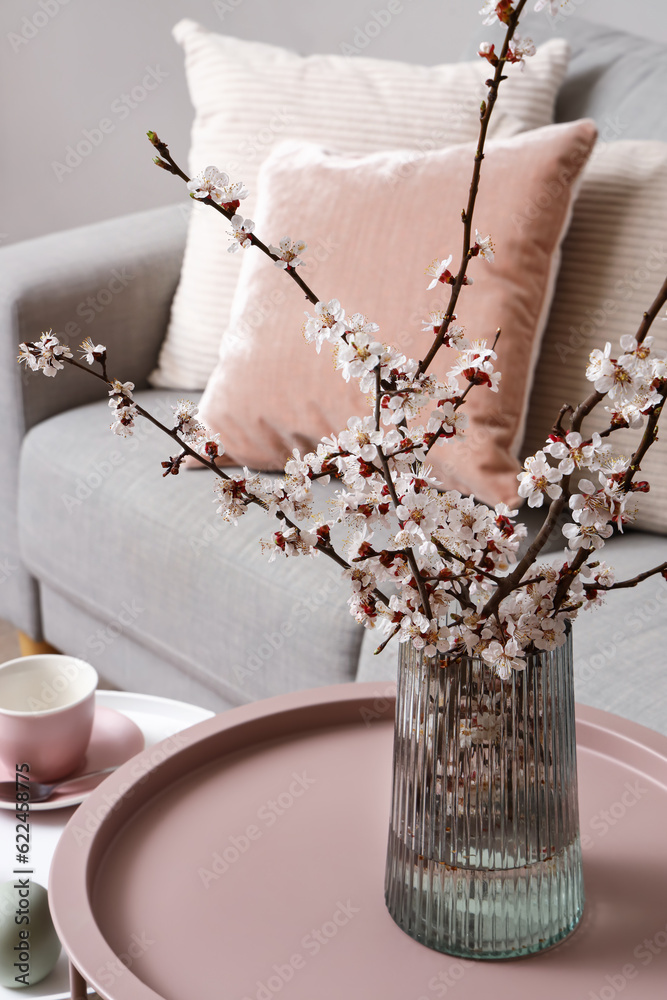 Vase with blooming tree branches on coffee table in living room, closeup