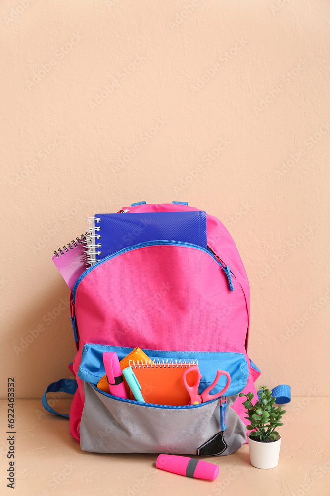 Color school backpack with notebooks, houseplant and markers on table near beige wall