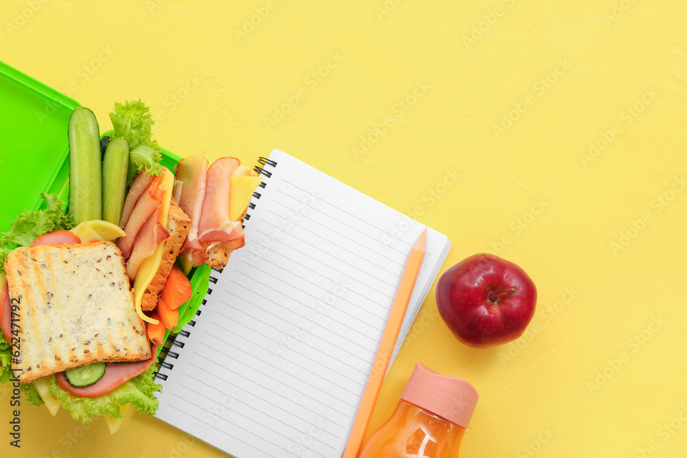 Stationery, drink and lunch box with tasty food on yellow background
