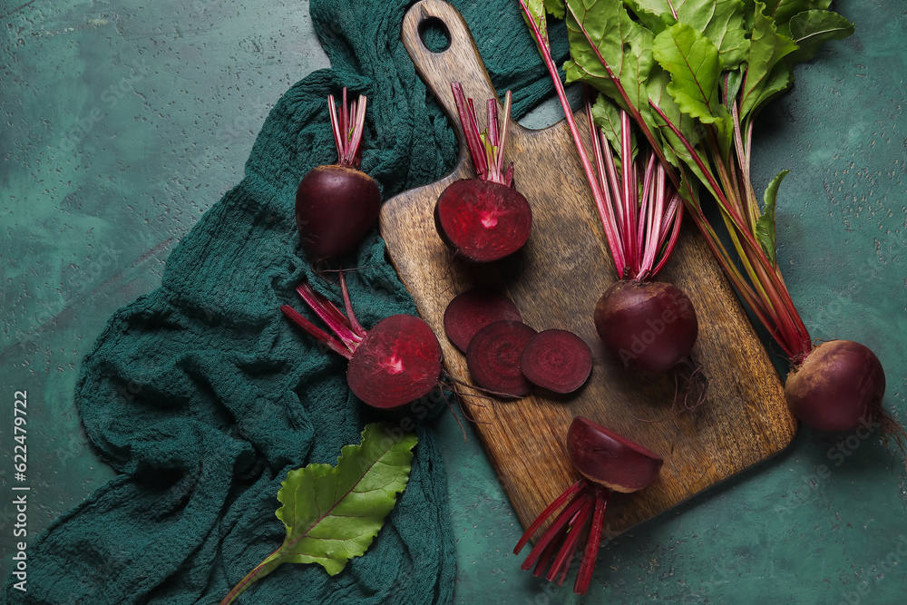 Wooden board of fresh beets with leaves on green background
