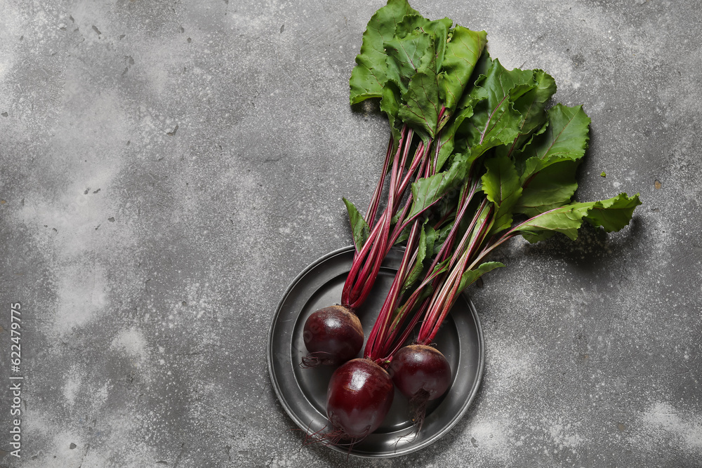 Plate of fresh beets with green leaves on grey background