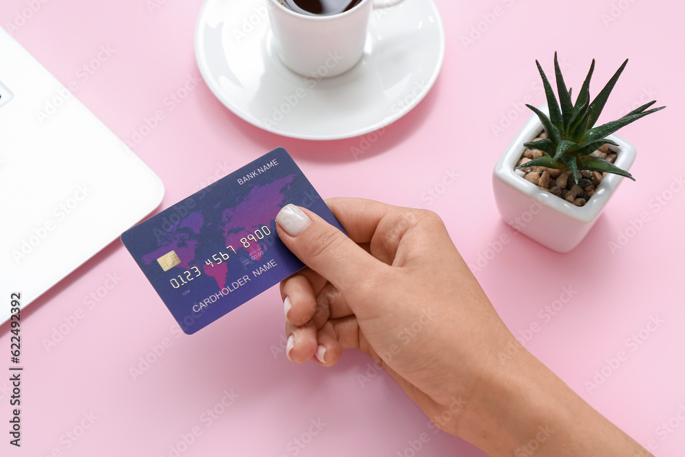 Female hand with credit card and cup of coffee on pink background