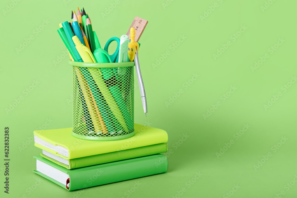 Holder with stationery and books on green background