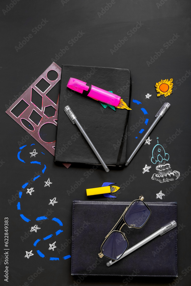 Creative composition with rockets, eyeglasses and different stationery on black chalkboard