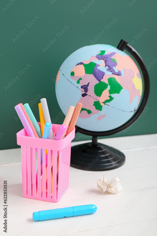 Different stationery with globe on white table against green chalkboard