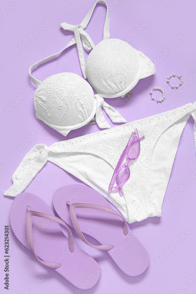 Stylish swimsuit, flip-flops, sunglasses and earrings on lilac background, closeup