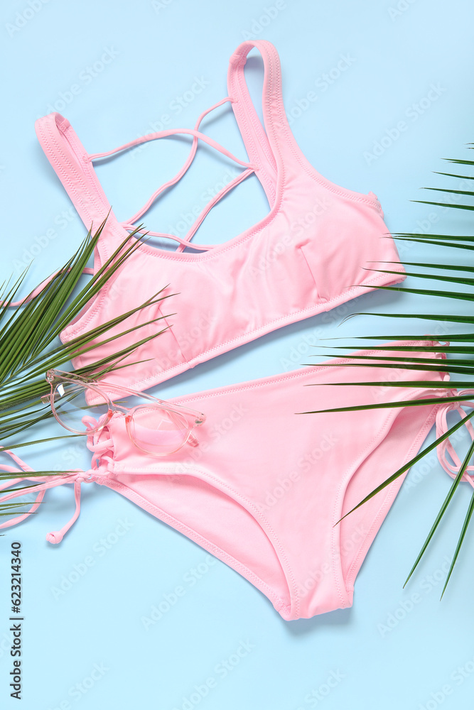 Stylish swimsuit and palm leaves on color background