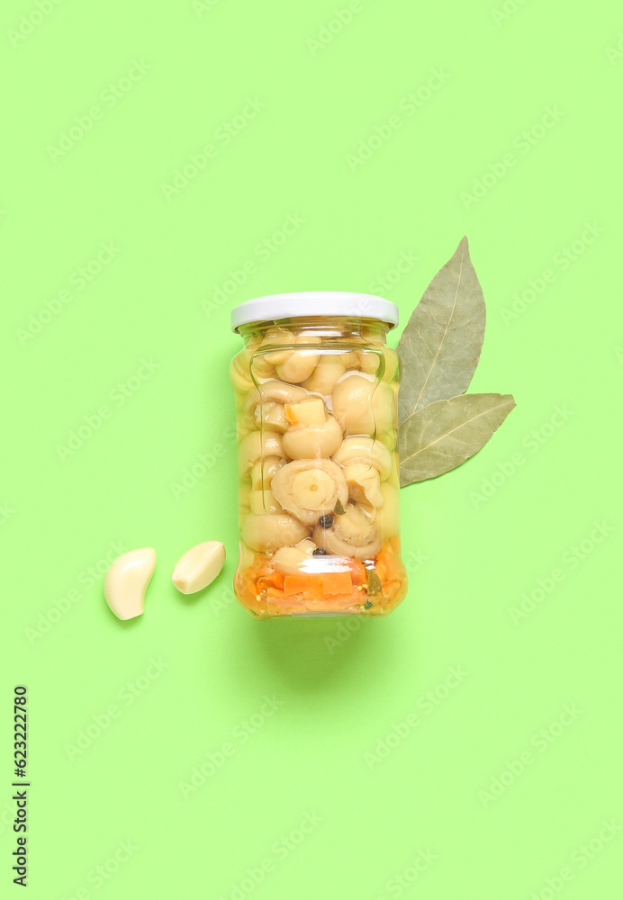 Jar with canned mushrooms on green background