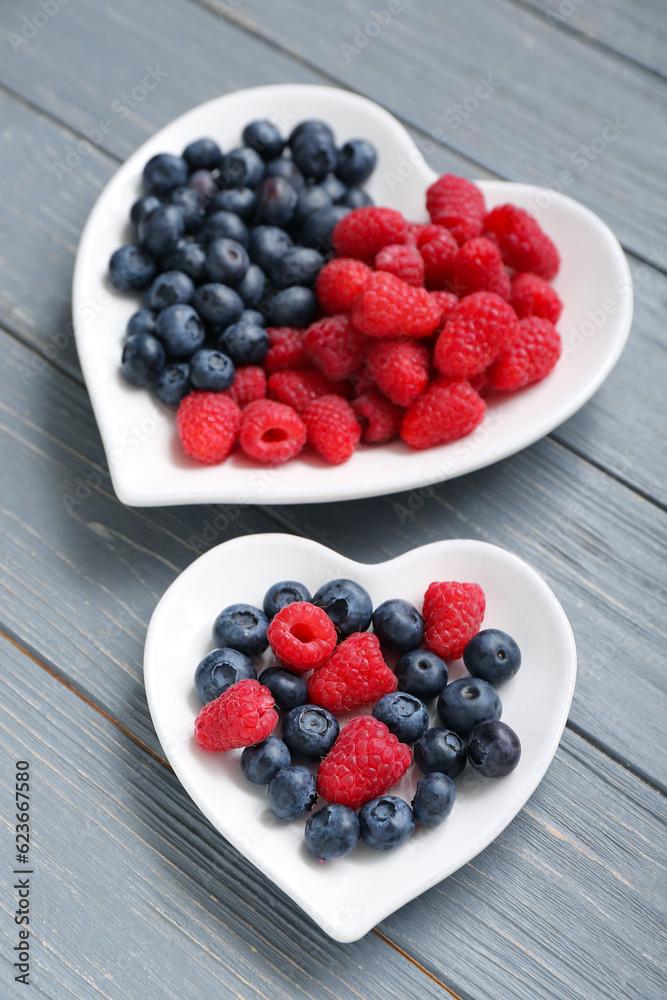 Plates with different fresh berries on grey wooden background, closeup