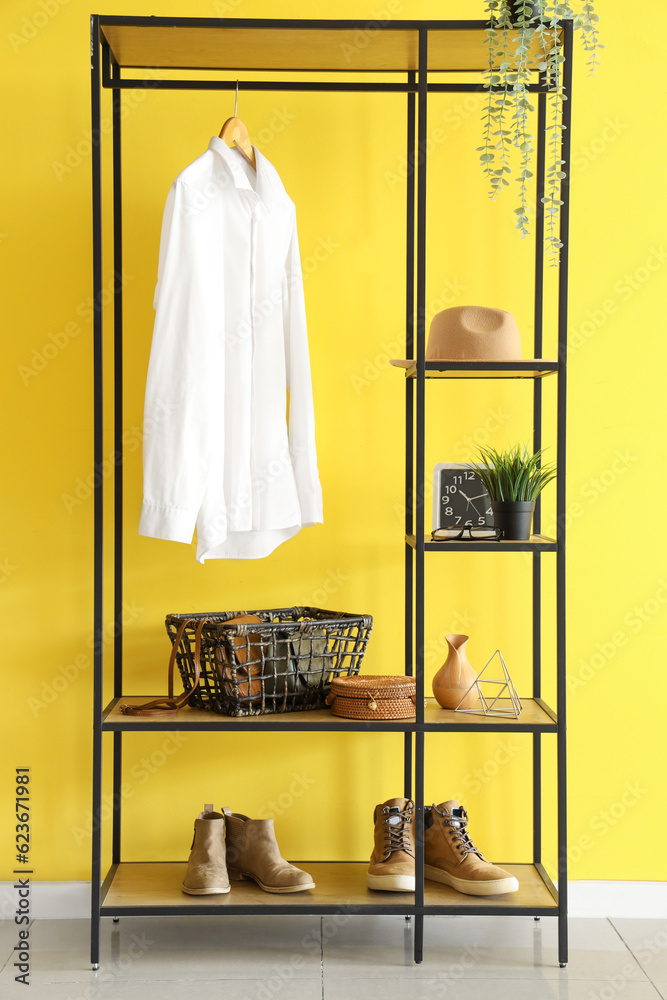 Shelving unit with white shirt, purses in basket, shoes and hat near yellow wall