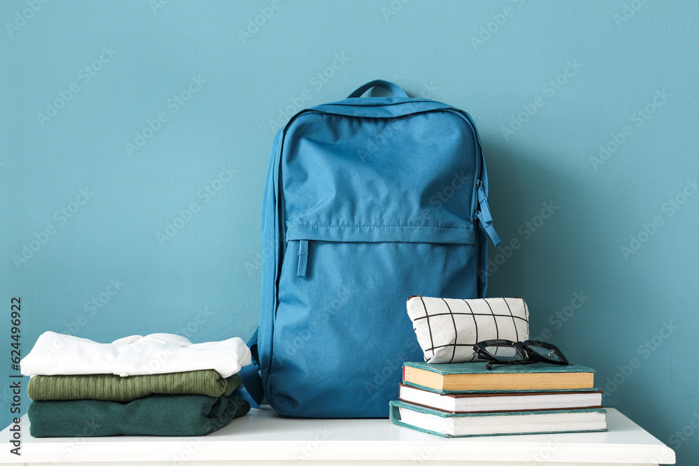 Table with stack of stylish school uniform, backpack, books, eyeglasses and pencil case near blue wa