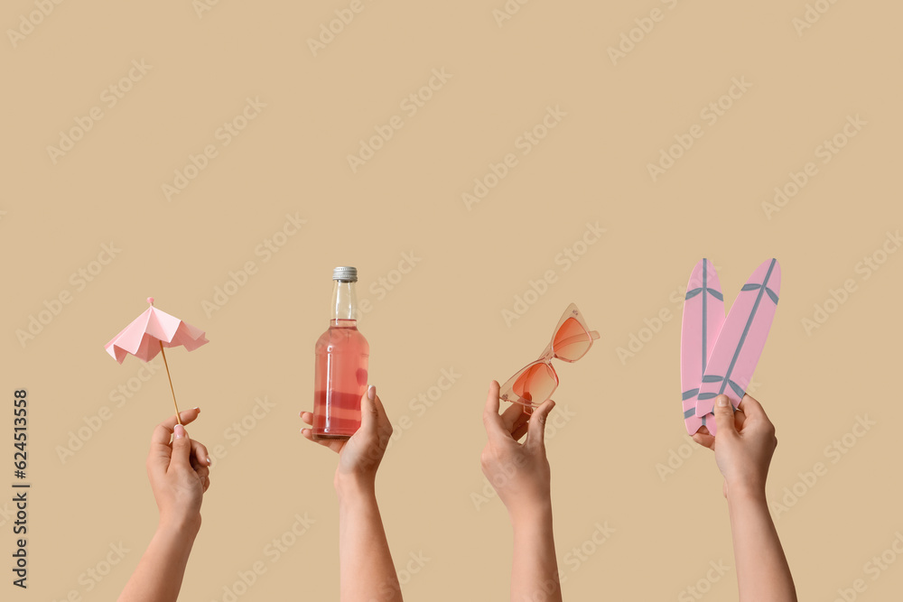 Female hands with beach accessories and bottle of cocktail  on beige background