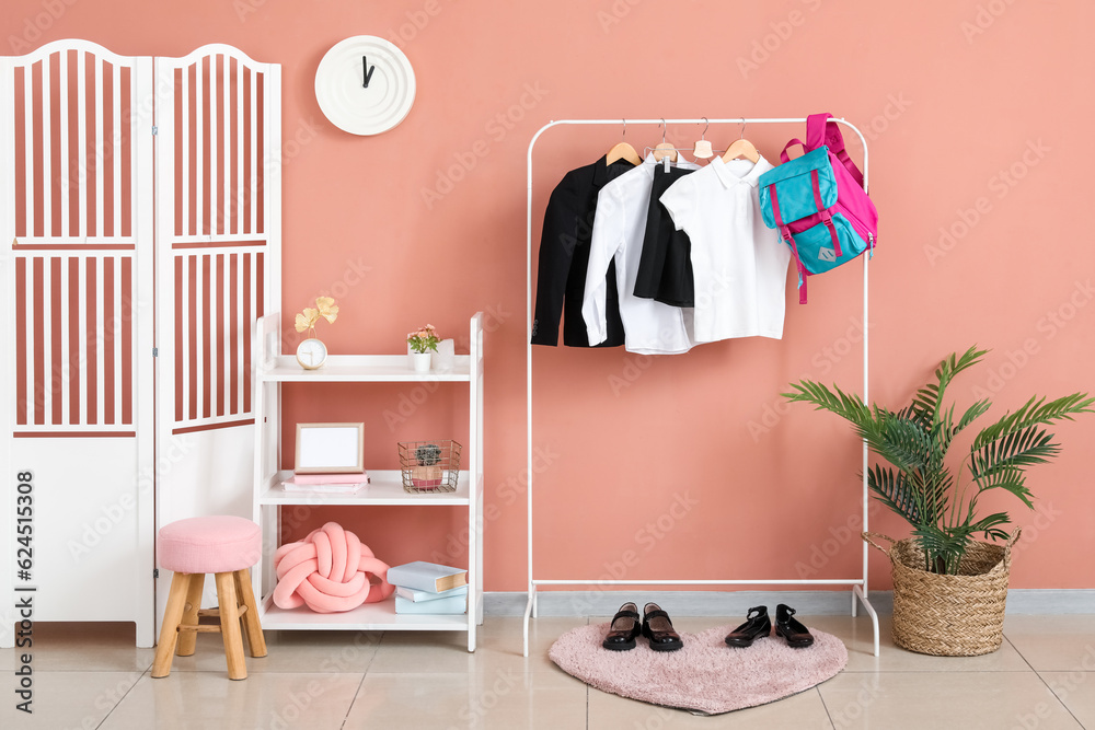 Rack with stylish school uniform, backpack, shoes, shelving unit and folding screen near beige wall 