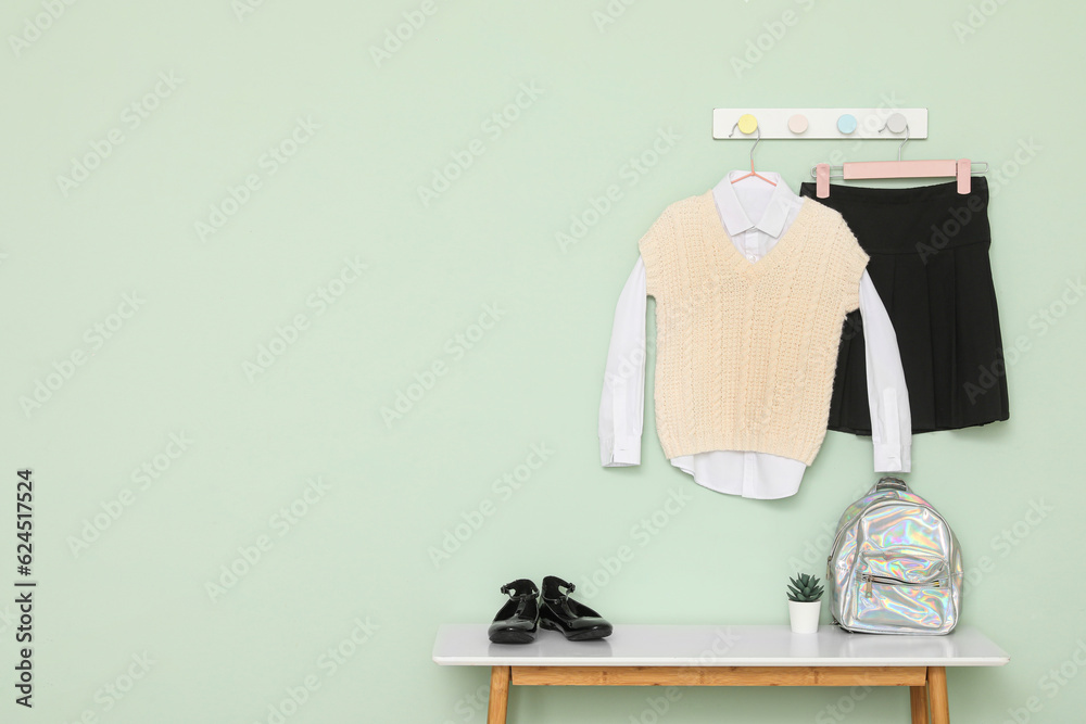 Stylish school uniform hanging on color wall, shoes and backpack