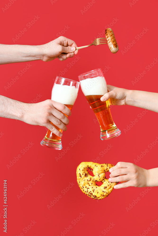 Many hands with glasses of cold beer, sausage and pretzel on red background