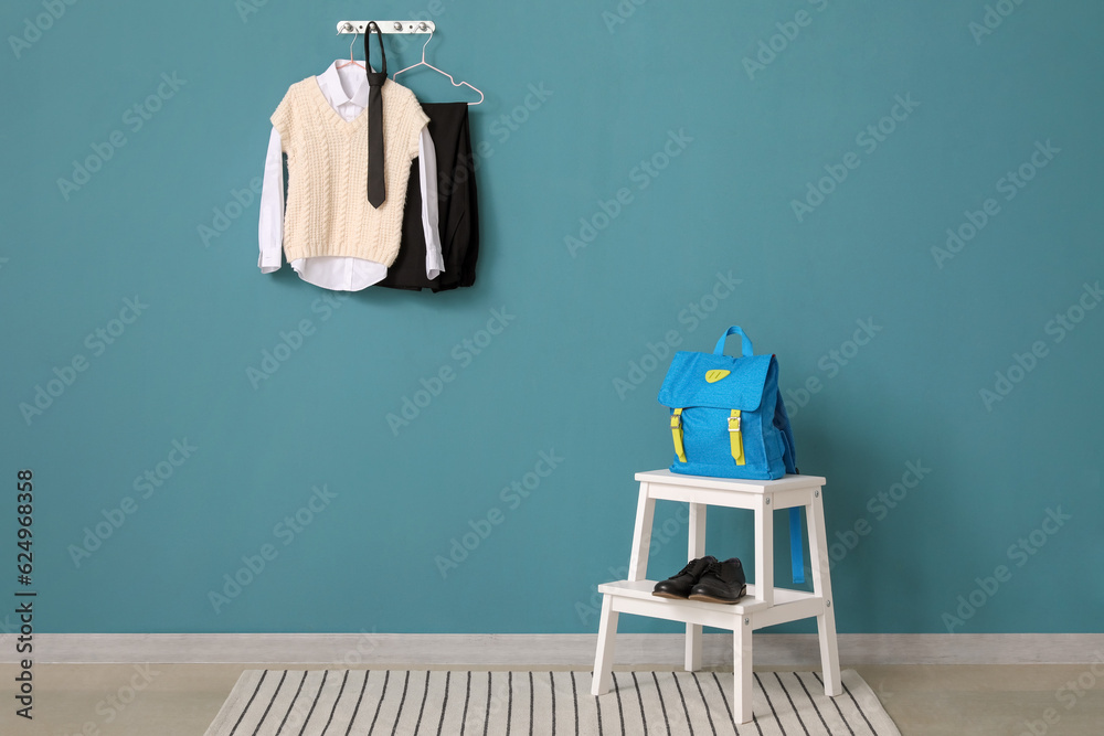Step ladder with school backpack, shoes and uniform hanging on color wall