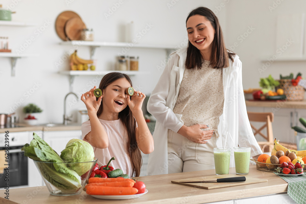 Little girl with her pregnant mother drinking green smoothie in kitchen