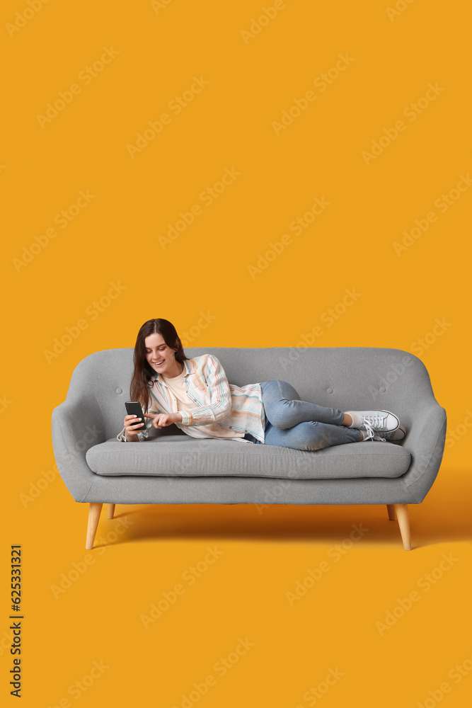 Young woman using mobile phone on sofa against yellow background