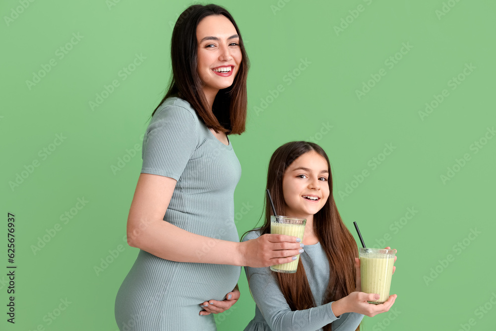 Little girl with her pregnant mother drinking smoothie on green background