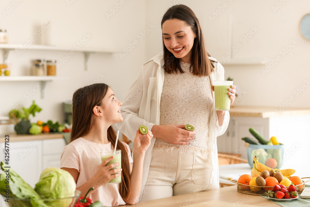 Little girl with her pregnant mother drinking green smoothie in kitchen