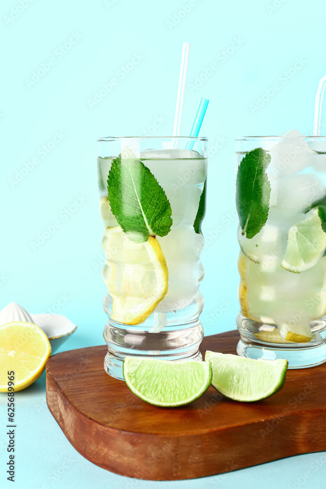 Wooden board with glasses of cold mojito and citrus fruits on color background, closeup