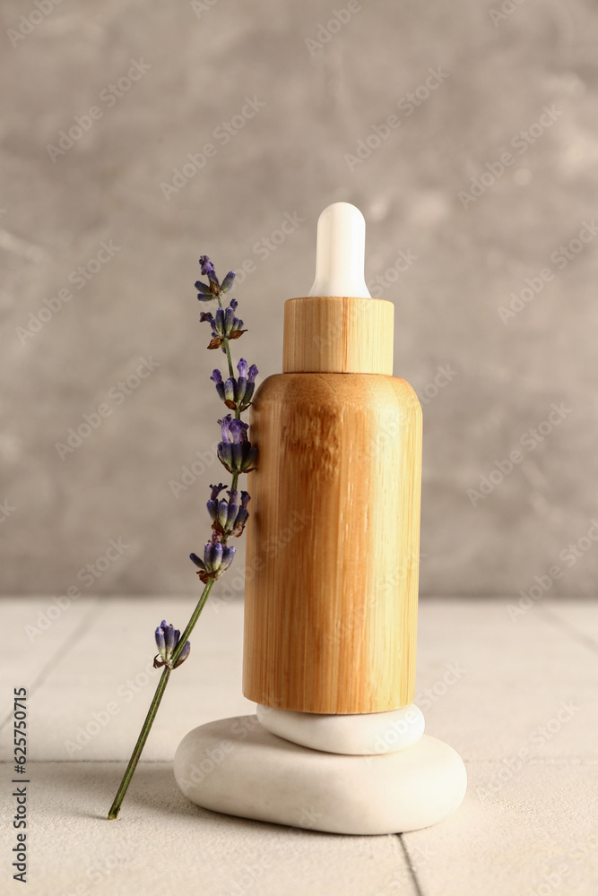 Composition with bottle of essential oil, spa stones and lavender flower on light tile table
