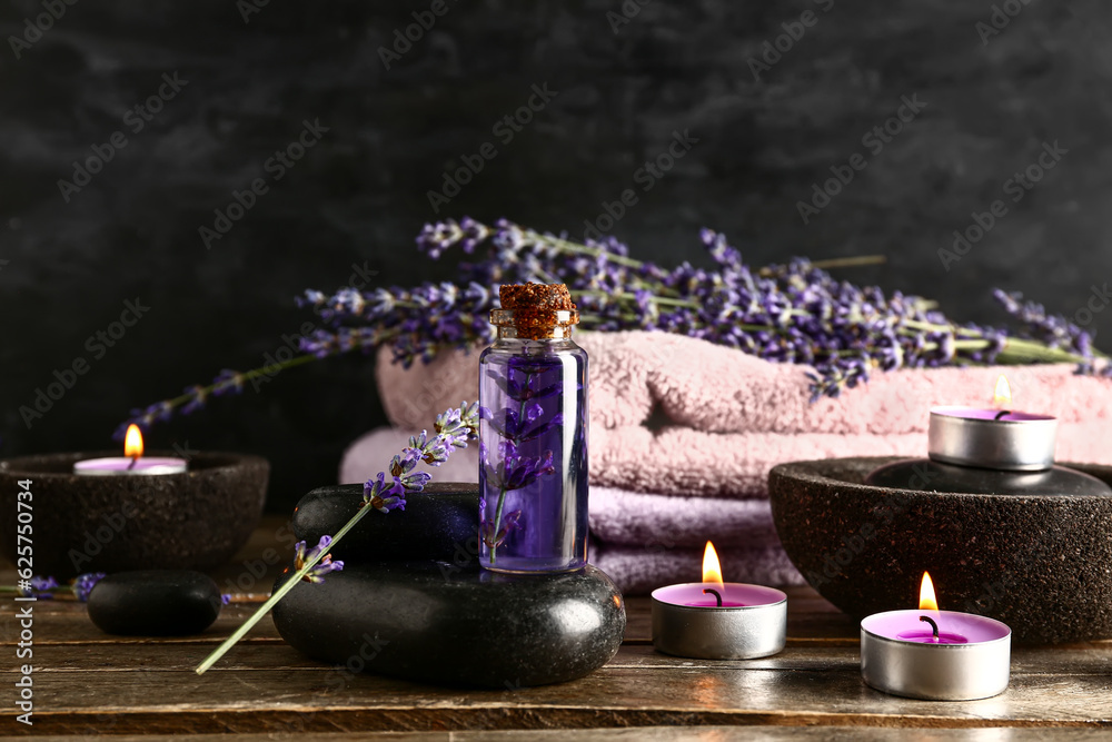 Composition with bottle of essential oil, spa stones, burning candles and lavender flowers on wooden