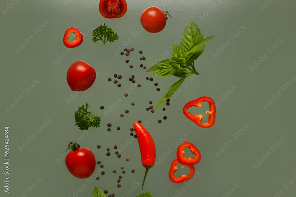 Flying peppercorns, vegetables and herbs on green background