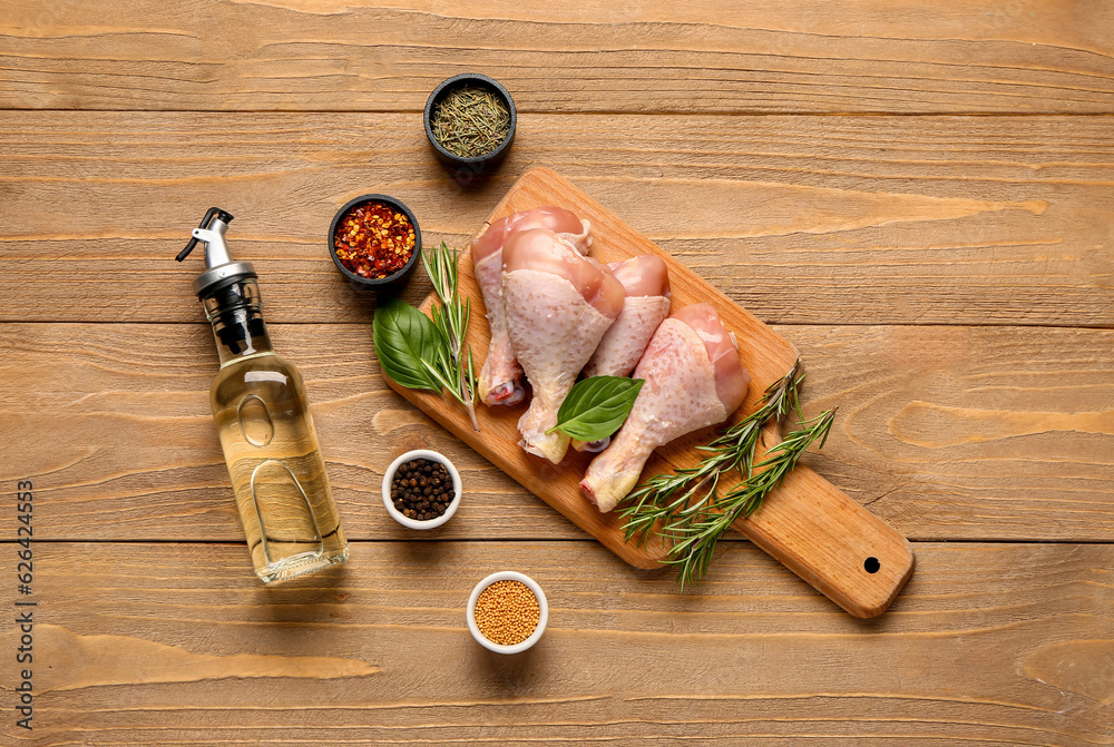 Cutting board with raw chicken legs, herbs, spices and oil on wooden background