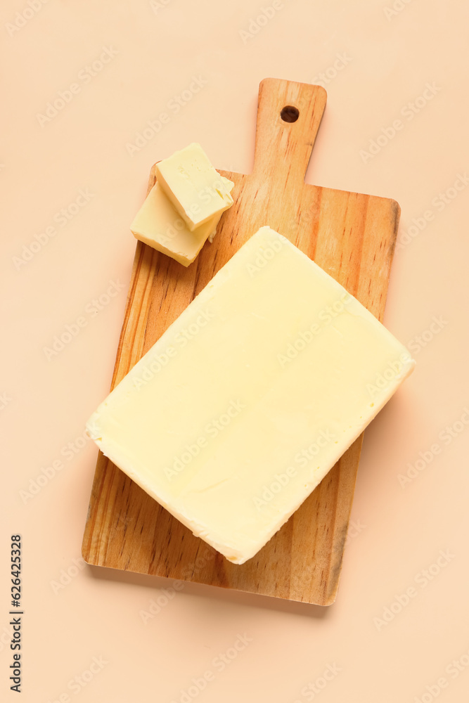 Wooden board with fresh butter on orange background