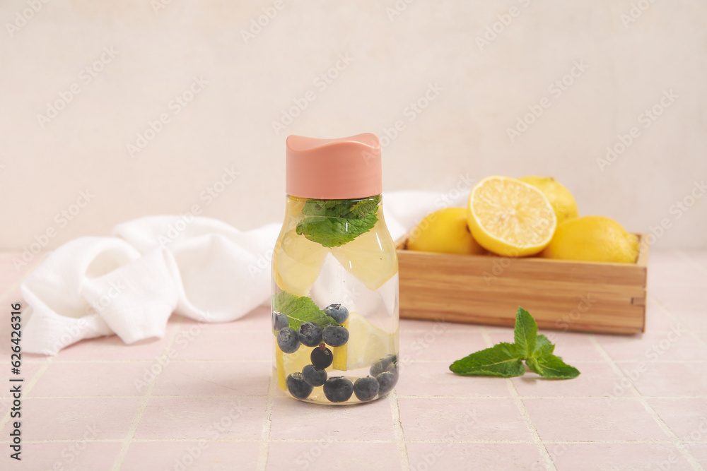 Sports bottle of infused water with lemon and blueberries on pink tile table