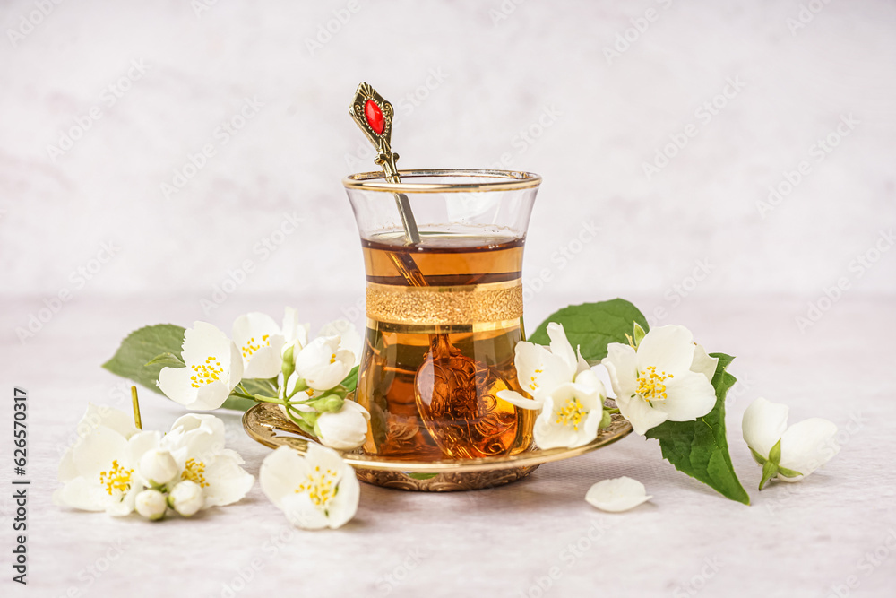 Cup of tasty aromatic tea and beautiful jasmine flowers on light background