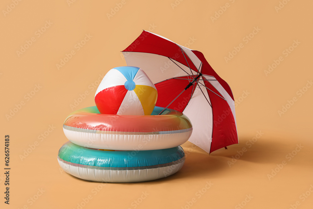 Swim rings with beach ball and umbrella on beige background