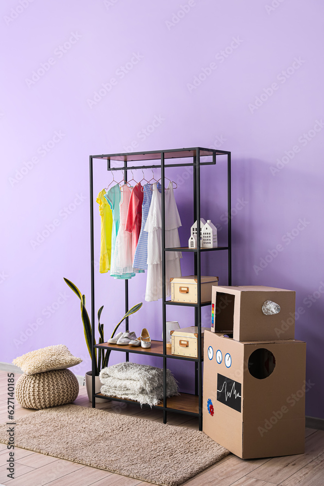 Shelving unit with childrens dresses and shoes near lilac wall in room
