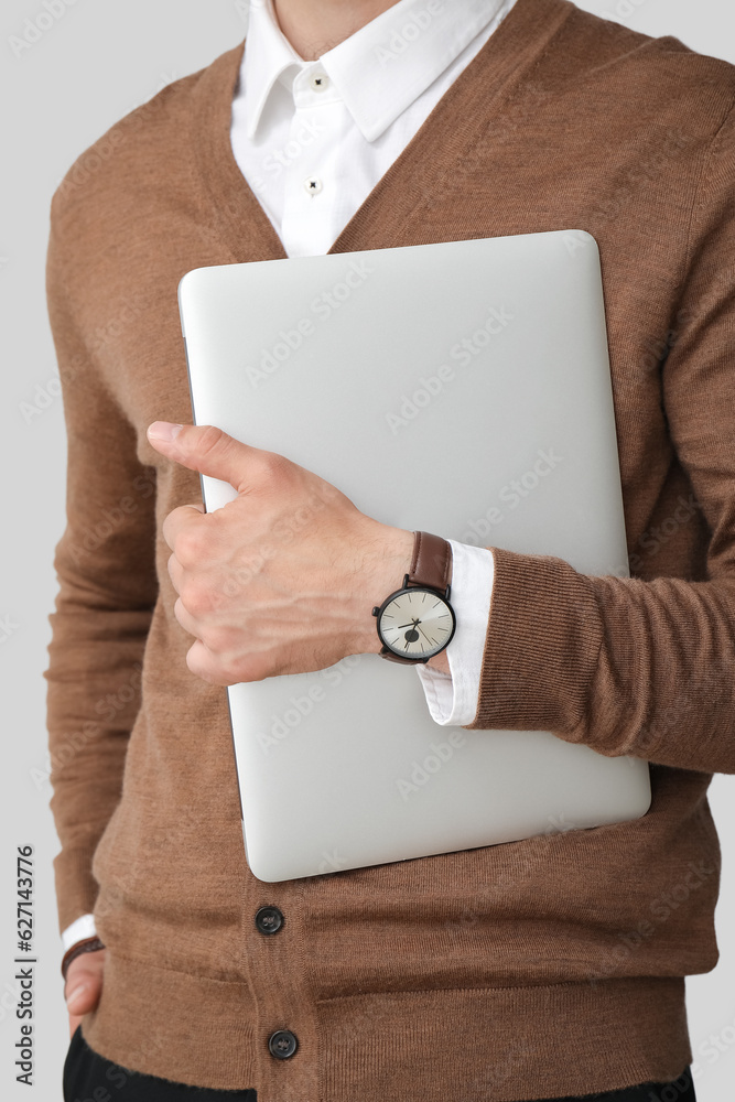 Handsome stylish young man with wristwatch and laptop on grey background