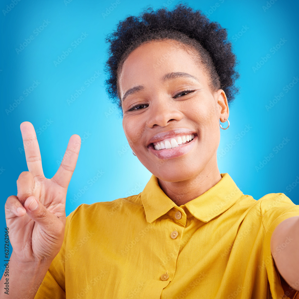 Happy woman, portrait smile and peace sign for selfie, photography or memory against a blue studio b
