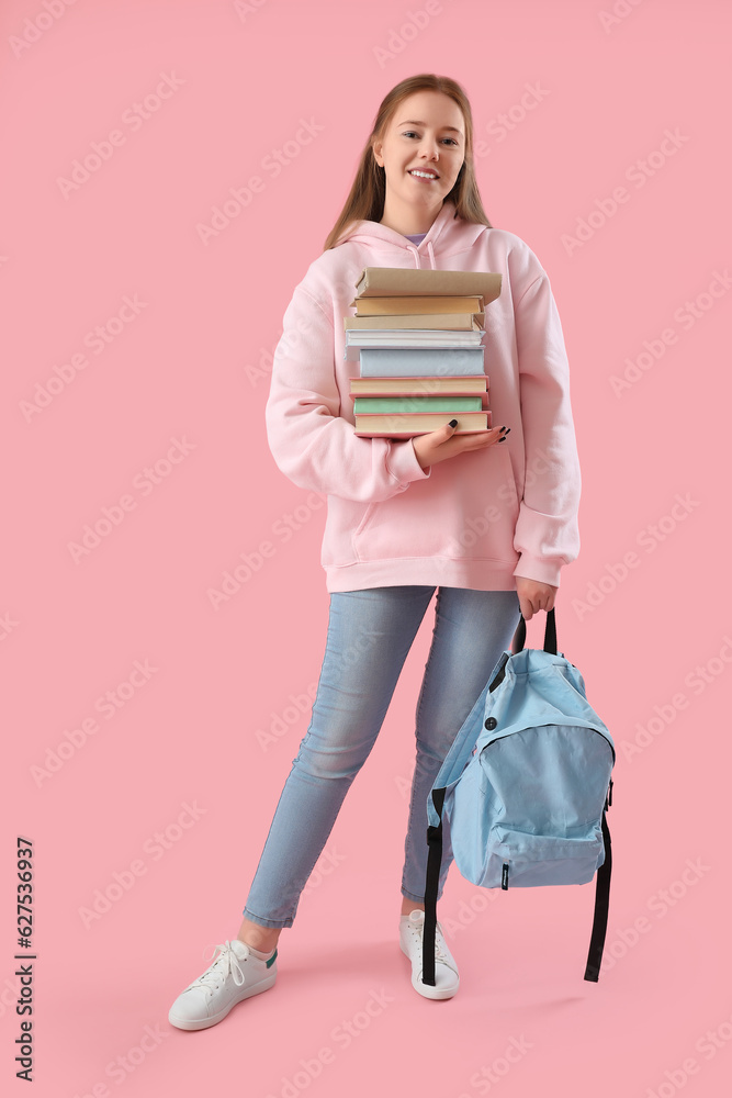 Female student with stack of books on pink background