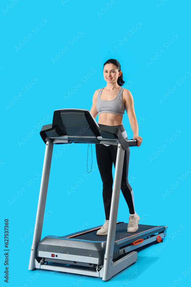 Beautiful woman training on treadmill against blue background