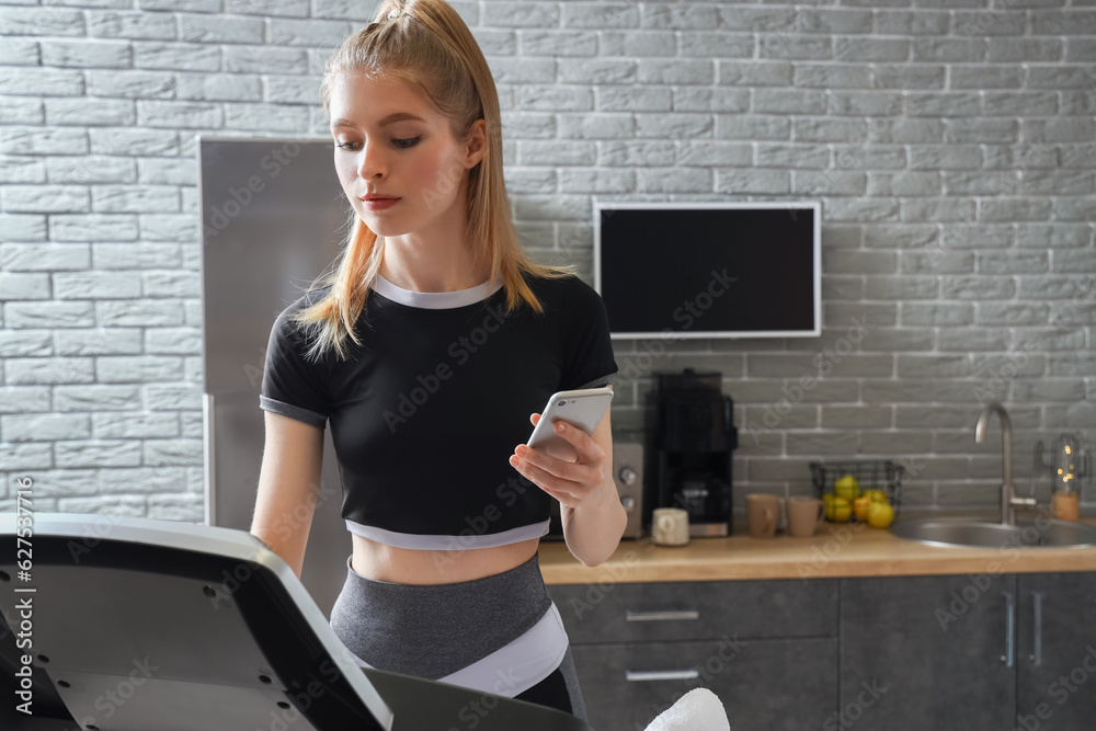 Sporty young woman with mobile phone training on treadmill at home