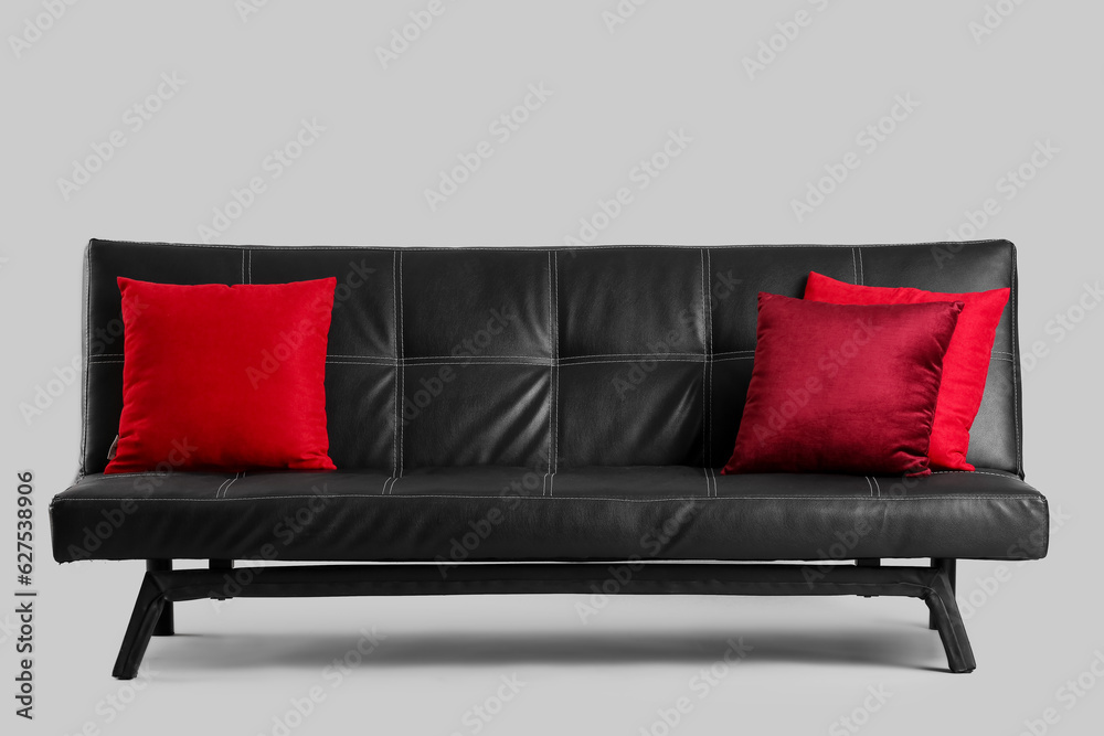 Stylish black sofa with red cushions on grey background