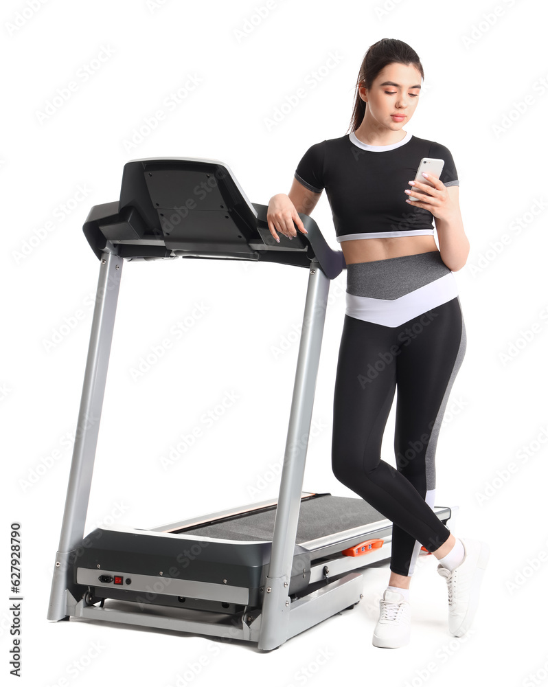 Sporty young woman with treadmill using mobile phone on white background