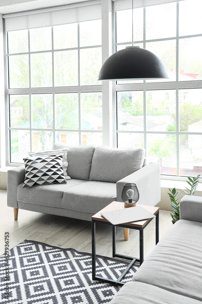 Interior of light living room with grey sofas, modern laptop on coffee table and big window