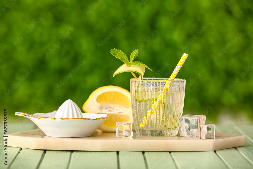 Glass of lemonade with cucumber and juicer on green wooden table outdoors